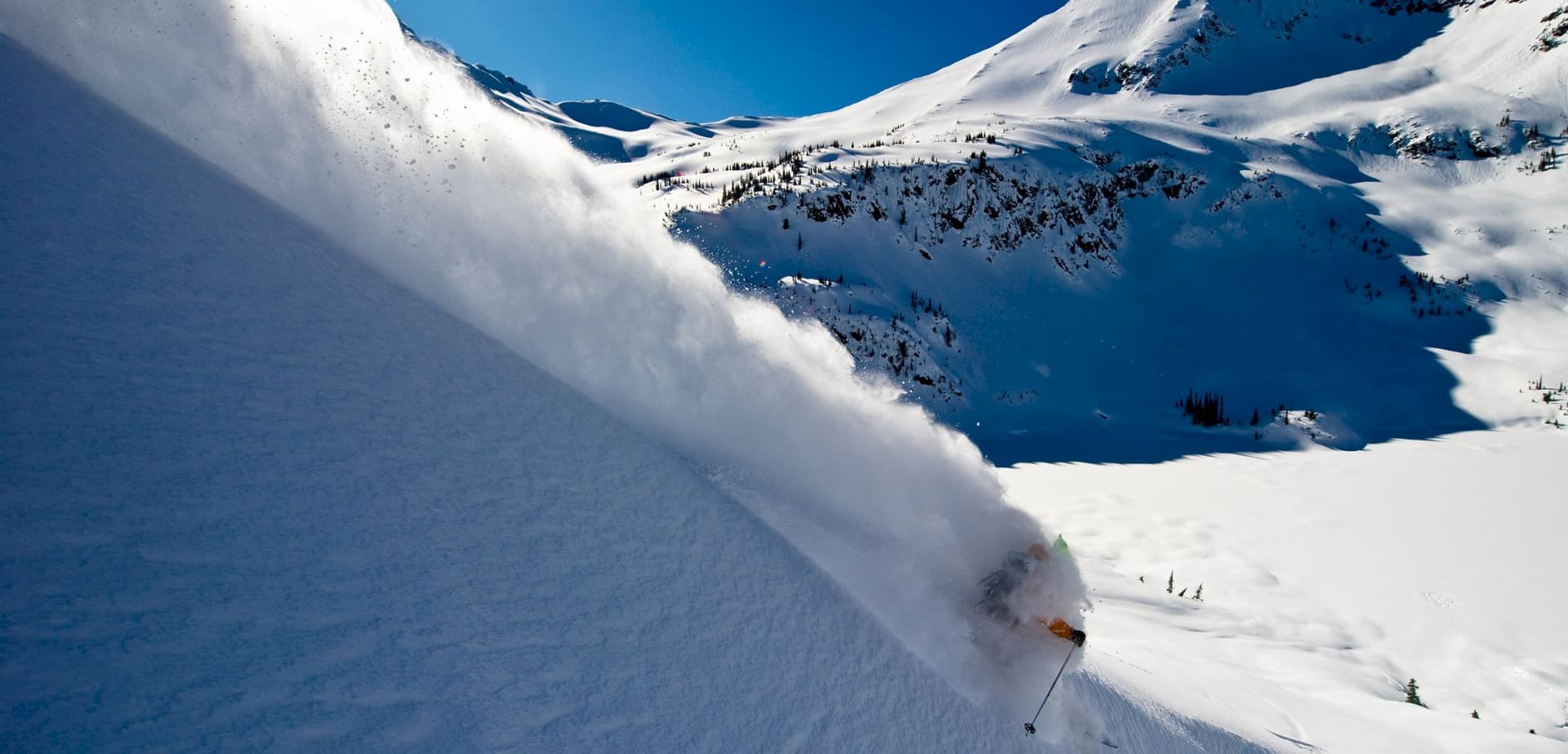 A thrilling winter sports scene at Tyax Heliskiing in British Columbia where a skier is dynamically swishing down the snowy slopes with mountains in the backdrop.
