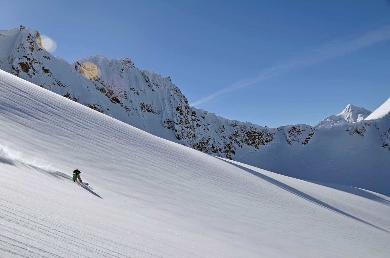 A skier takes on the frosty slopes at Tyax Heliskiing in Vancouver, surrounded by fellow enthusiasts. A quaint chalet and sprawling ski resort are visible in the background.