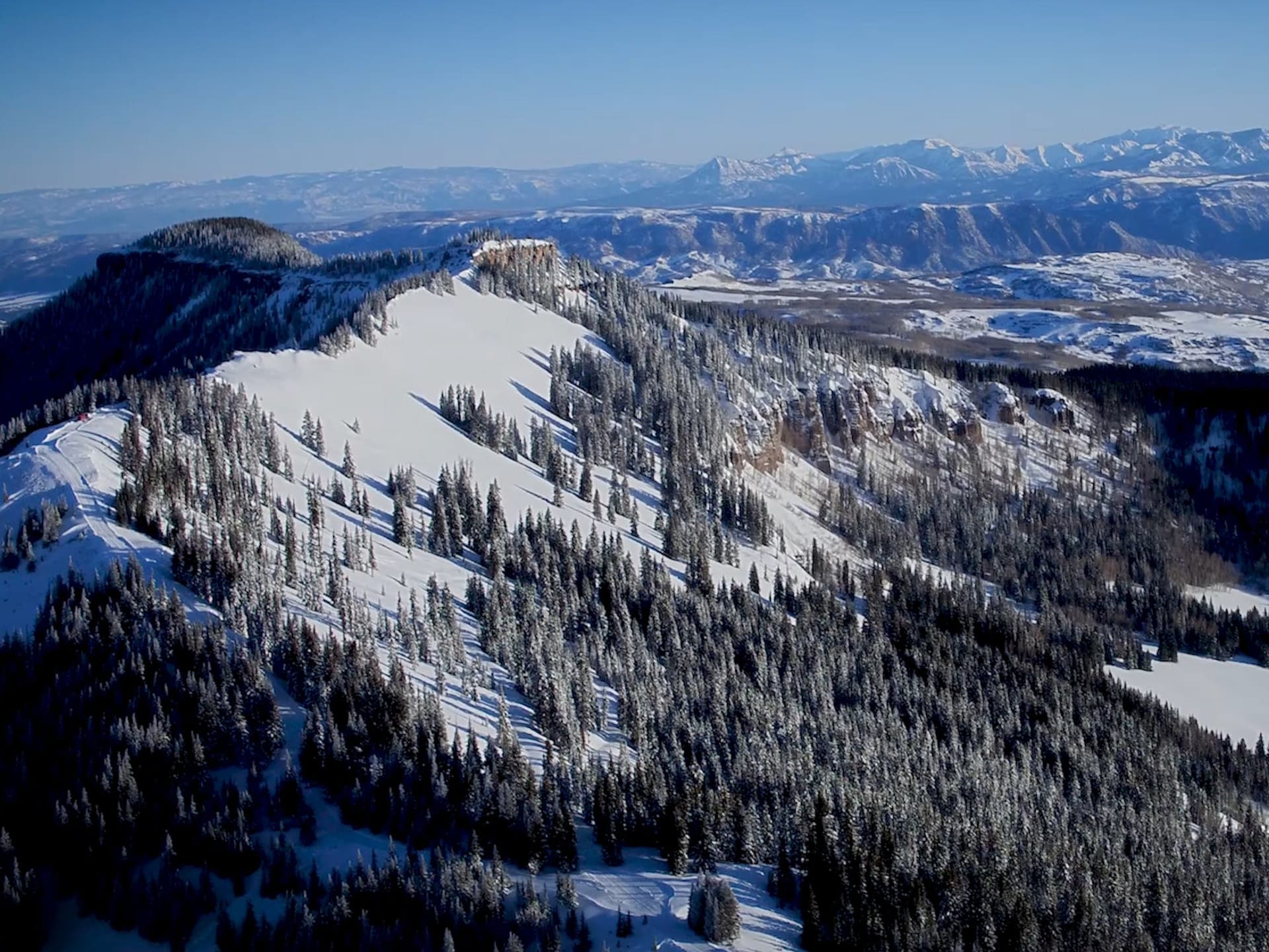 A ski resort at Cimarron Mountain Club in Colorado, featuring snow-covered slopes bustling with winter sports activities against the stunning backdrop of a mountain.