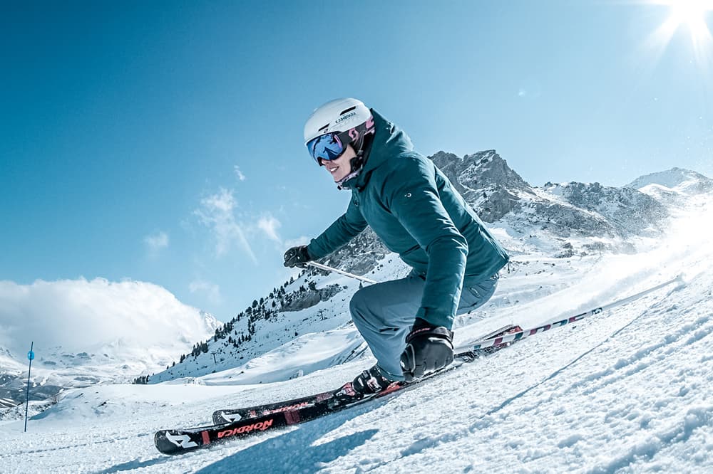 A skier gliding down a snow-covered slope in Panticosa, Aragon, Huesca, Spain. The scene reveals a bustling winter sports centre, hinting at the lively atmosphere of the ski resort.