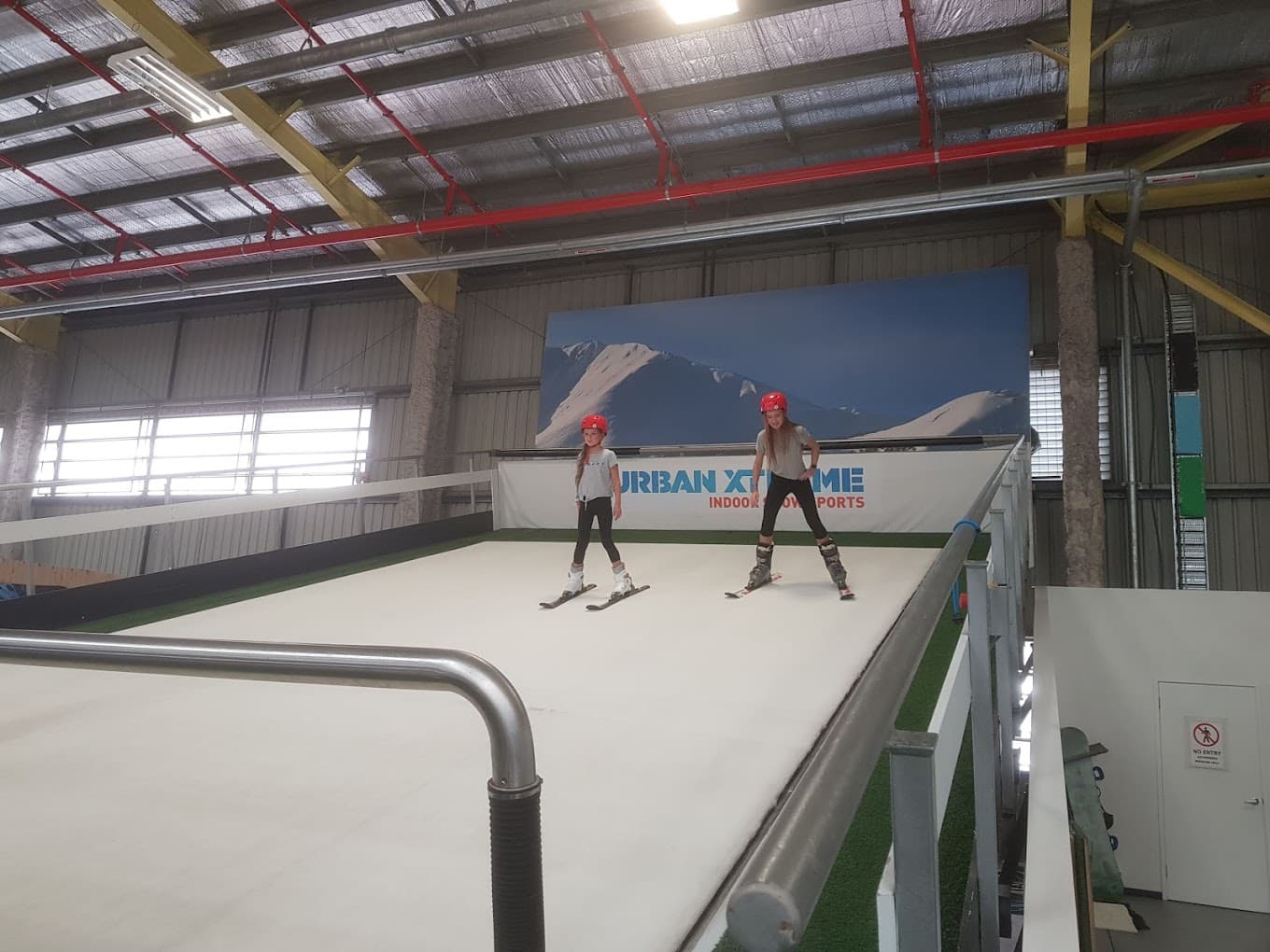 Image of a vibrant winter sports centre at Urban Xtreme in Queensland, Australia. The scene includes a skier and possibly a snowboarder in action, with a charming challet in the background.