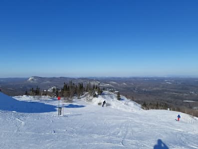 A winter scene at Mont-Orford ski resort in Quebec Canada featuring a skier a ski lift and a mountain covered in snow.