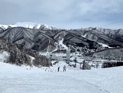 A picturesque view of Naeba ski resort in Japan, displaying a captivating winter scene. Snow-covered slopes are filled with winter sports enthusiasts, eliciting a lively but serene atmosphere.