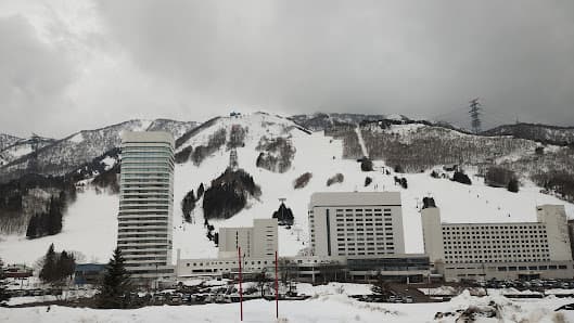 Scenic view of Naeba ski resort in Niigata, Japan, featuring stunning winter landscape, bustling winter sports activities and a ski lift traversing the resort.