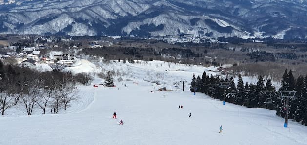 A beautiful winter scene at Myoko Akakura Kanko ski resort in Honshu, Japan featuring scenic snow-covered slopes with crisp, white snow. Skiers elegantly navigate through the stunning landscape.