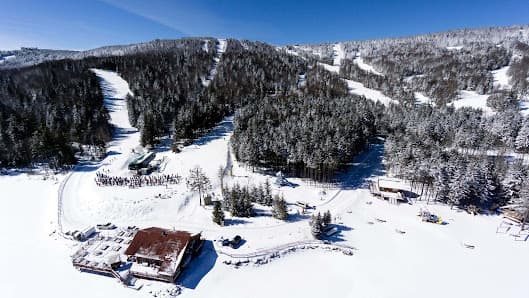Scenic view of Collet ski resort in Allevard, France featuring snowy slopes, a rustic chalet, and lively winter sports activities under a clear blue sky.