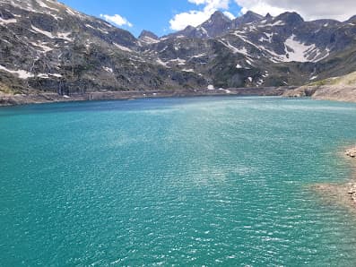 View of the serene lake near the Petit train d'Artouste in France's Pyrénées-Atlantiques. A quaint chalet overlooks the water, nested against the backdrop of majestic mountains.