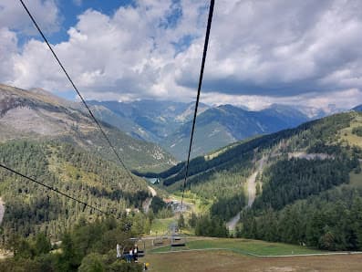 A ski lift ascending up the mountainside in La Colmiane France. Nearby is a quaint chalet with the vast ski resort stretching out in the background. A lone skier can be seen in the distance.