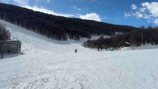 A skier enjoys a run on the snowy slopes of Tsaghkadzor ski resort, Armenia with a charming challet and a ski lift in the background, depicting a bustling winter sports scene.