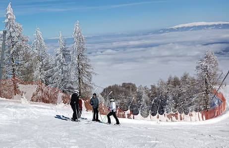 A bustling winter scene at Roc d'Enfer ski resort in France featuring a group of people and a family enjoying skiing on the snow-covered slopes against a stunning backdrop of Mont Blanc.
