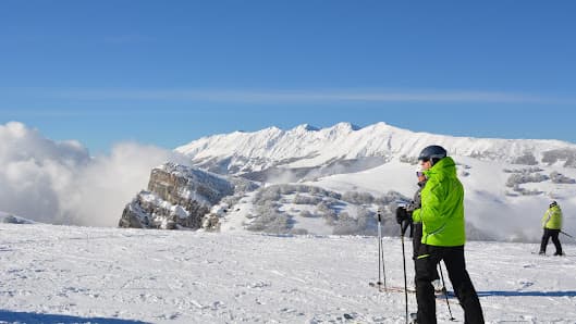 A skier enjoys the snow at Altopiano di Brentonico ski resort in Italy with a charming chalet in the background providing a picturesque winter sports scene.