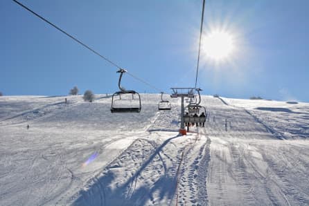 A scenic winter view of Altopiano di Brentonico ski resort in Italy featuring a bustling ski lift skiers enjoying the slopes and a charming chalet nestled in the snow.