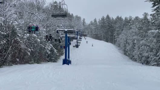 A vibrant winter sports scene at Pats Peak, Henniker, NH, featuring a ski lift in action, a bustling ski resort surrounded by stunning winter scenery, and skiers enjoying the slopes.