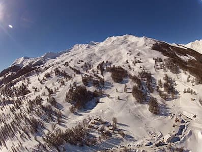 Winter scene at Sainte-Anne la Condamine ski resort in France, showcasing a charming chalet, activity on the snow-covered slopes, and majestic mountain backdrop.