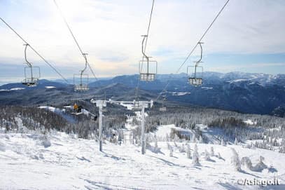 A skier enjoying a day on the snow-covered slopes of Sciovie Verena ski resort in Vicenza Italy with a ski lift visible in the background.
