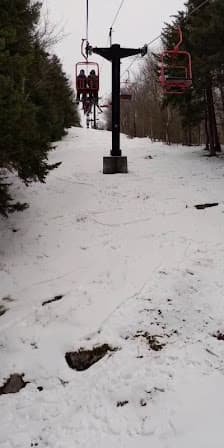 A skier glides down the slopes of Magic Mountain in Londerry Vermont. A ski lift runs up the snowy landscape. This winter sports scene captures the essence of a day at the ski resort.