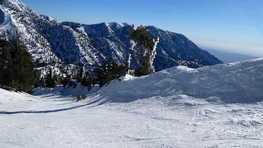 A skier enjoying a winter sport on a sunny day at Mt Baldy ski resort in California with a picturesque mountain in the background and stunning winter scenery around.