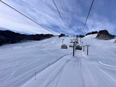 Ski resort scene at Chokai Kogen Yashima in Akita, Japan. Features a ski lift leading up to a challet amongst pristine white snow, with individuals engaging in various winter sports activities.