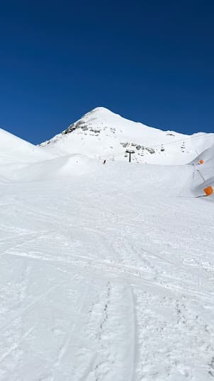 A skier enjoying a winter day on the slopes of Piancavallo ski resort in Italy with a chalet and mountain scenery in the background.