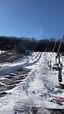 A winter sports scene at Shawnee Mountain Pennsylvania with a ski resort evident. A ski lift can be seen traversing the snow-covered slopes where a skier is also visible.