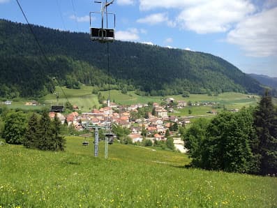 A sunlit chalet in Robella Val-de-Travers, Neuenburg, Switzerland stands against a scenic backdrop of mountains. A ski-lift and ski resort hint at the area's popular winter activities.