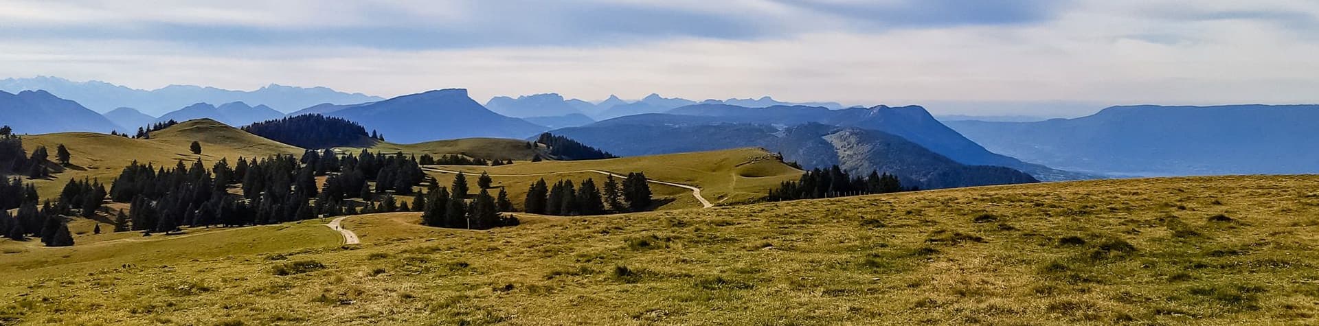 Station du Semnoz in France - a grassy hill with trees and mountains in the background.