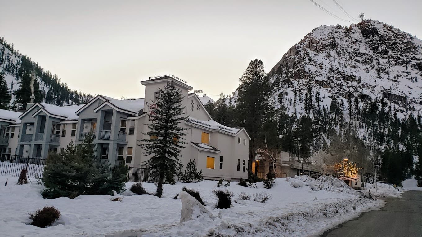 Winter scene at Palisades Tahoe in Lake Tahoe, California, showcasing clear skies, snowy mountains and a bustling ski resort teeming with winter sports enthusiasts.